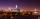 A city skyline at night. In the foreground is a river lined by trees, a glowing glass museum building and a bridge.
